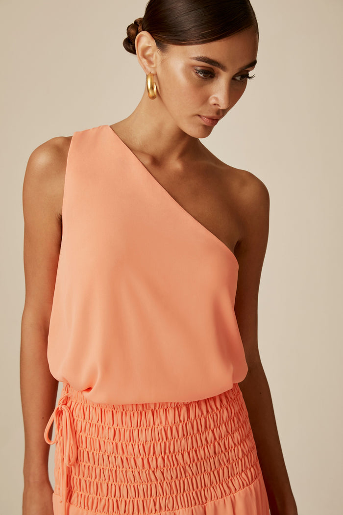 A female is wearing a one shoulder tank top with layered hemline.